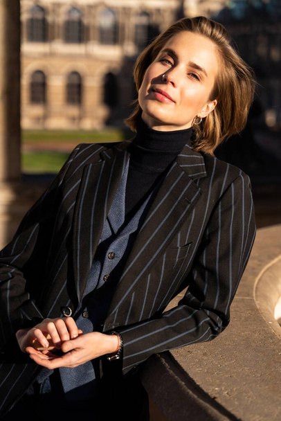 Young blond happy woman in striped jacket leaned on sunny historic building - Fotografie, Obrázek
