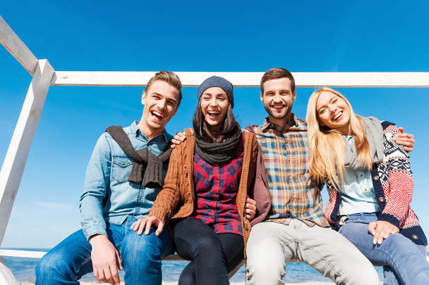 Four happy young people sitting at riverbank - Φωτογραφία, εικόνα
