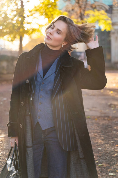Young blond short-haired woman in striped jacket, jeans and vest touches hair - Foto, immagini