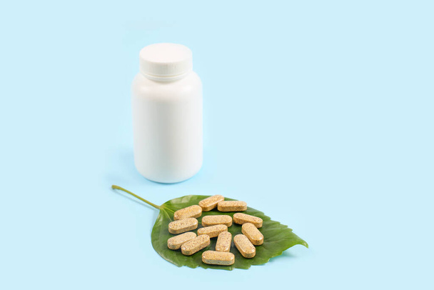 Bio-Pillen auf grünem Blatt und Glas auf blauem Hintergrund - Foto, Bild