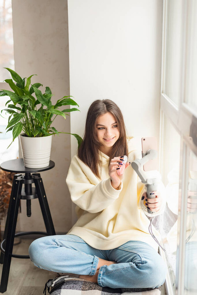 A young woman beauty blogger live broadcasted a review of cosmetics on social media. A modern female influencer shows off her daily makeup while talking to a smartphone camera. Soft selective focus. - 写真・画像