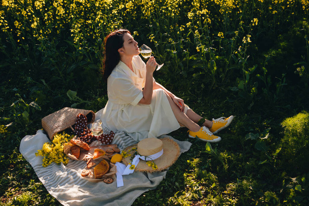 приголомшлива жінка в білій сукні, сидячи на ковдрі, п'є вино романтичне місце
 - Фото, зображення