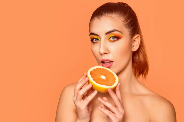 Closeup portrait of beautiful smiling girl , holding half of oranges near face, isolated on orange background. Beauty and health care concept. - Foto, immagini
