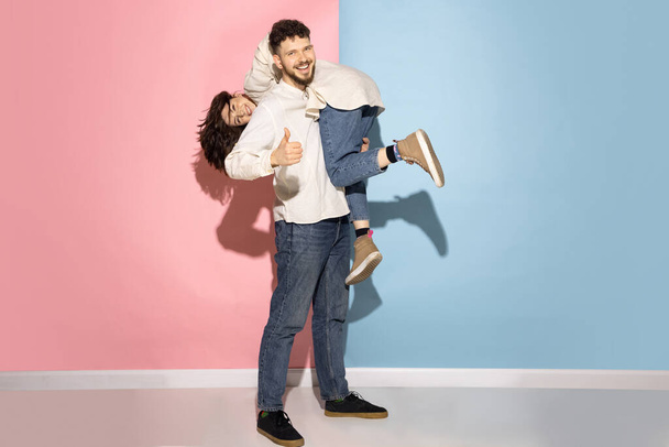 Emotional couple of young funny and happy man and girl having fun studio on blue and pink trendy color background. - Foto, Bild