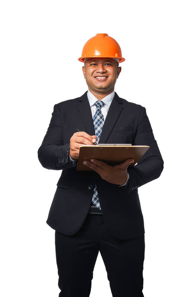 Retrato de engenheiro chefe bonito vestindo terno preto capacete laranja escrita prancheta isolada no fundo branco com caminho de recorte. - Foto, Imagem