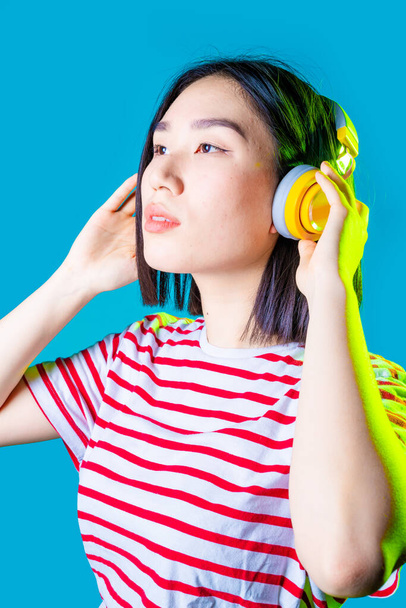 Mujer asiática joven aislada sobre fondo azul escuchando música auriculares inalámbricos de ensueño - Foto, Imagen