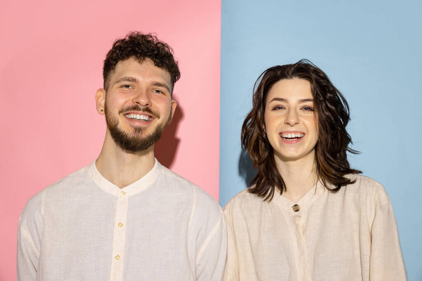 Half length portrait of young emotive man and girl looking at camera isolated on blue and pink trendy color background. Human emotions concept - Φωτογραφία, εικόνα