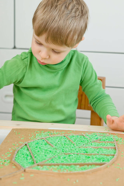 Boy plays with green color rice. Implement for children to develop fine motoric skills through play. DIY toy to learn hand - eye coordination. - Foto, Imagem