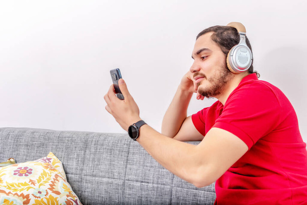 young man listening music with headphones and singing on sofa - Φωτογραφία, εικόνα