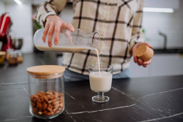 Mutfakta bardağa badem sütü döken bir kadın. Sağlıklı vegan ürün konsepti. - Fotoğraf, Görsel