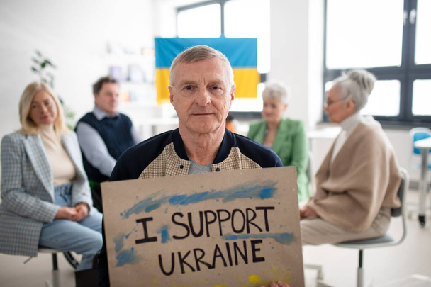 Group of seniors showing support when praying for Ukraine together in church community center. - Foto, afbeelding