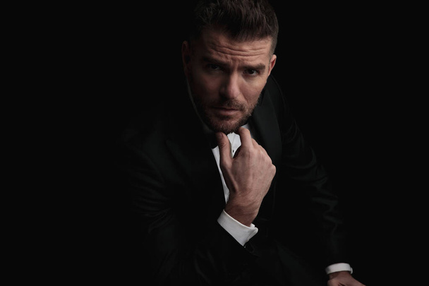 elegancki stylowy mężczyzna po czterdziestce trzymając się za podbródek i myśląc przed czarnym tle w studio - Zdjęcie, obraz