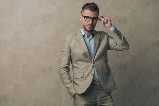 jonge zakenman houdt een hand in zak, het repareren van zijn bril in een mode pose - Foto, afbeelding