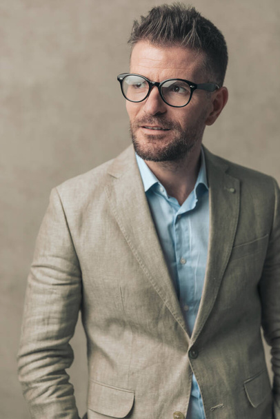 portret van een knappe zakenman met een bril en een pak, wegkijkend in een mode pose - Foto, afbeelding