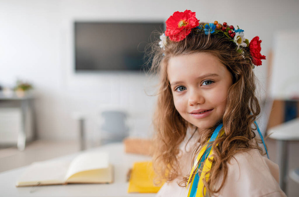 Little happy Ukrainian girl looking at camera in classroom, concept of enrolling Ukrainian kids to schools. - 写真・画像