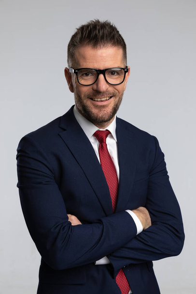 happy businessman with eyeglasses smiling and crossing arms on grey background  - Valokuva, kuva