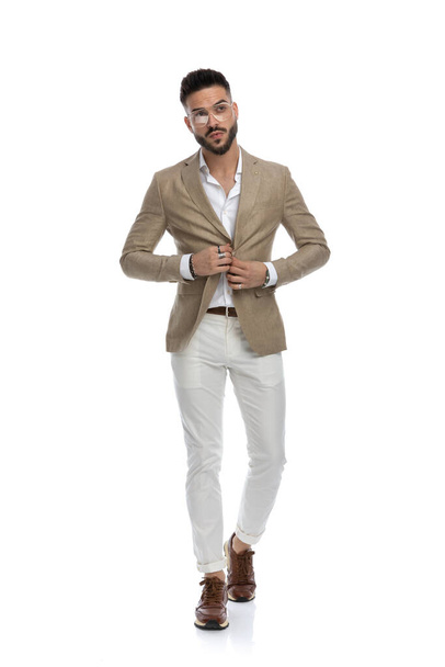 smart casual man unbuttoning his jacket, walking to the camera and looking away on white background - Photo, Image