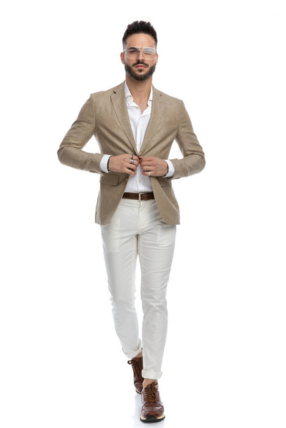 homem de negócios atraente andando enquanto organiza sua jaqueta com atitude difícil no fundo branco - Foto, Imagem