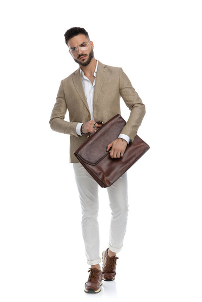 atractivo hombre de negocios llevando su maletín con actitud dura y mirando a la cámara sobre fondo blanco - Foto, Imagen