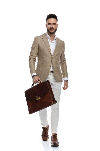 ハンサムなビジネスマンは厳しい態度で歩き白を背景にブリーフケースを持ち - 写真・画像