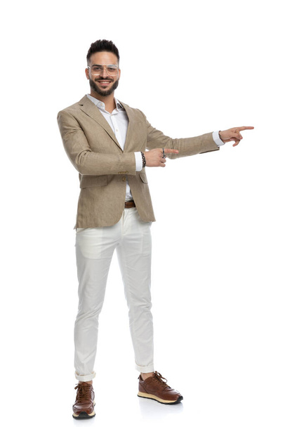 empresário sexy apontando para o lado, sorrindo para a câmera e vestindo óculos no fundo branco - Foto, Imagem