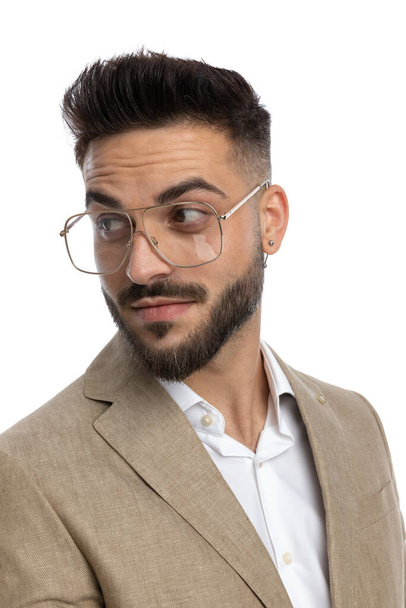 bonito empresário olhando para trás sobre ombro com um sorriso sutil e vestindo óculos no fundo branco - Foto, Imagem