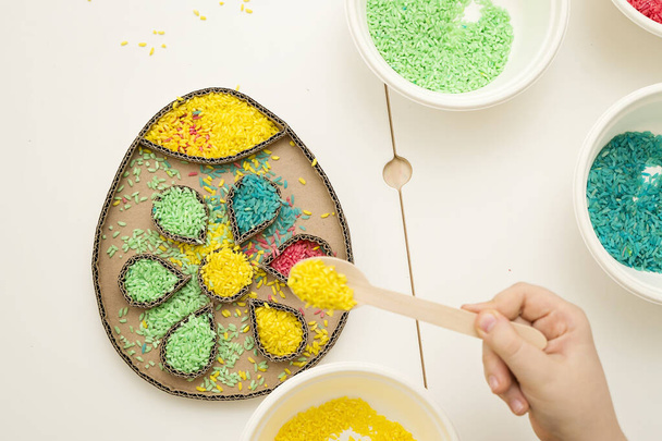 Decorating an Easter egg with colored rice. A tool for children to develop fine motor skills while playing. DIY toy for hand-eye coordination. - Photo, Image