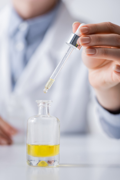 bijgesneden weergave van laboratoriumassistent die pipet in de buurt van fles met serum houdt - Foto, afbeelding
