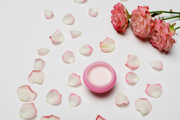 high angle view of pink flowers and petals near small container with cream on white - Fotoğraf, Görsel