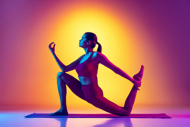 Портрет молодої спортивної дівчини тренування, виконання розтяжок і вправ йоги ізольовані над градієнтним рожевим і жовтим тлом в неоні
 - Фото, зображення