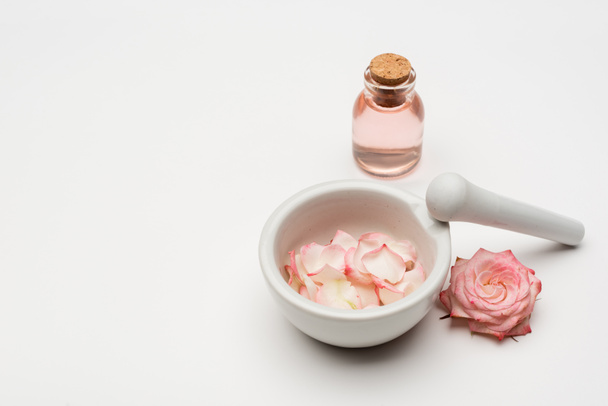 flower near pestle and mortar with petals and bottle with rose water on white - Photo, Image