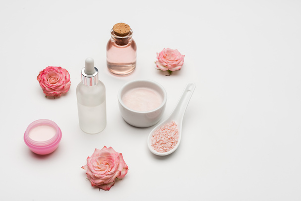 květiny v blízkosti mořské soli, sérum a láhev s růžovou vodou na bílém - Fotografie, Obrázek