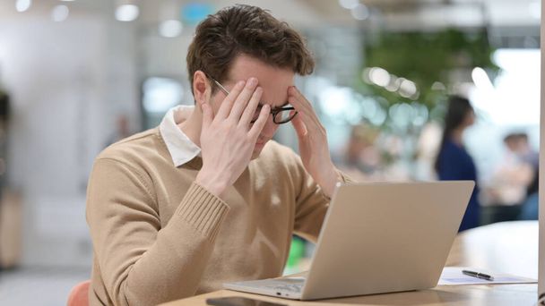 Hombre joven que tiene dolor de cabeza mientras trabaja en el ordenador portátil  - Foto, imagen