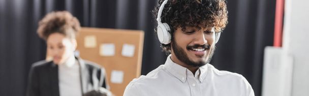 Positive indian businessman in headphones in office, banner  - Foto, Bild