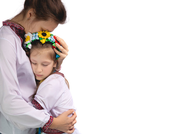 La mère étreint l'enfant avec des yeux larmoyants. Un enfant en vêtements nationaux ukrainiens. Photo studio sur fond blanc. - Photo, image