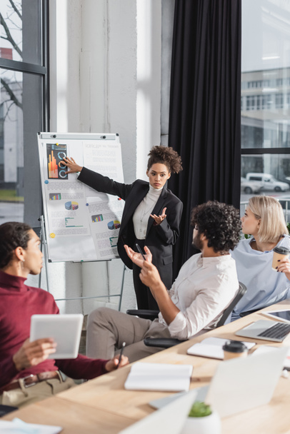 African american businesswoman pointing at flip chart near interracial colleagues during meeting in office  - Photo, Image