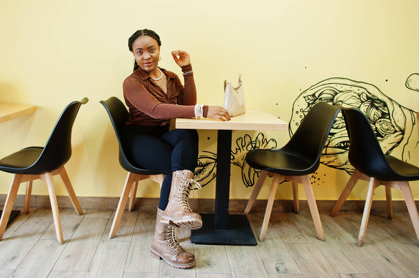 African american woman in brown shirt and black pants sit in cafe. - Zdjęcie, obraz