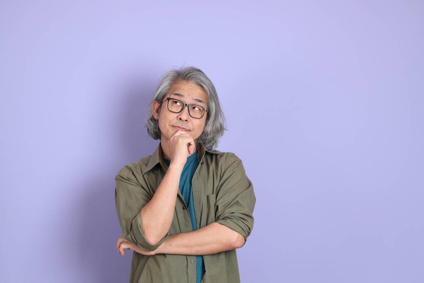 Starší asijský muž s ležérní oblečení stojící na fialovém pozadí. - Fotografie, Obrázek