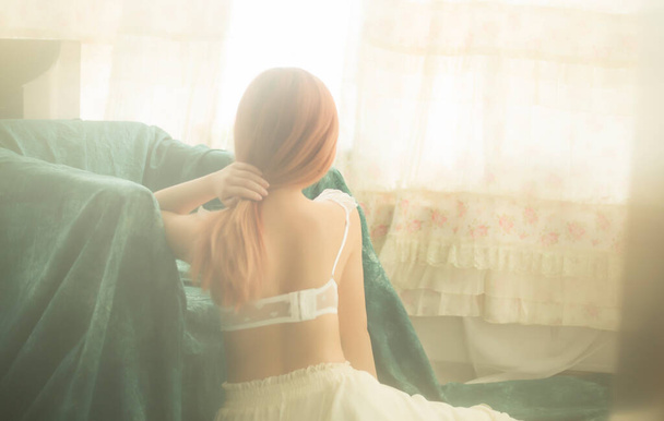 belle jeune femme aux cheveux longs en robe blanche assise sur le lit dans la chambre - Photo, image