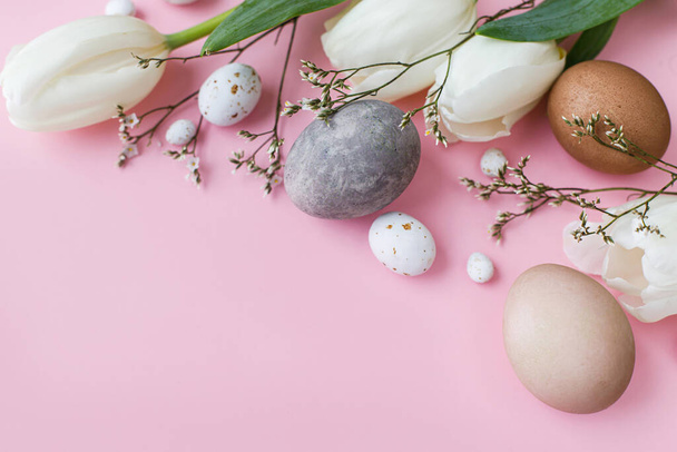 Stylish eggs, tulips flat lay on pink background. Modern natural dyed easter eggs and white tulips layout. Greeting card template, easter background. Space for text. Happy Easter! - Photo, Image