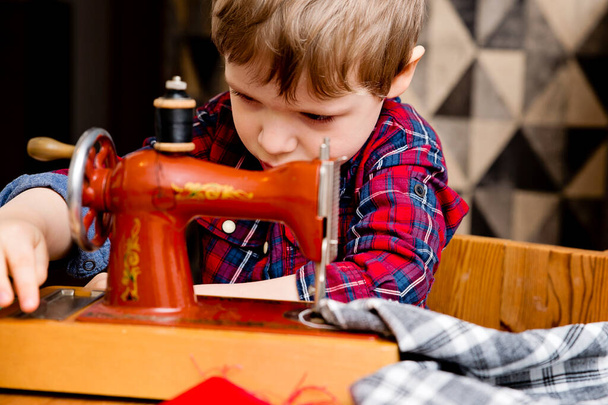 Learning professions. Boy sewing clothes with a mechanical hand sewing machine. Retro toy, reduced copy of original. Activities at home. Artistic mimic of real professional. - Photo, image