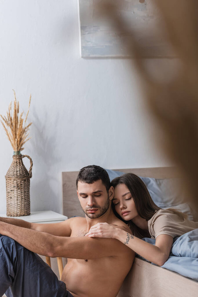 Brunette woman with closed eyes touching muscular man in bedroom  - Fotoğraf, Görsel