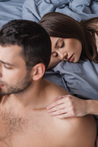 High angle view of pretty woman touching shoulder of shirtless boyfriend in bedroom  - Photo, Image