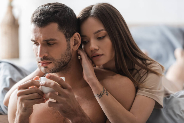 Pretty brunette woman touching sexy boyfriend with cup of coffee in bedroom  - Zdjęcie, obraz