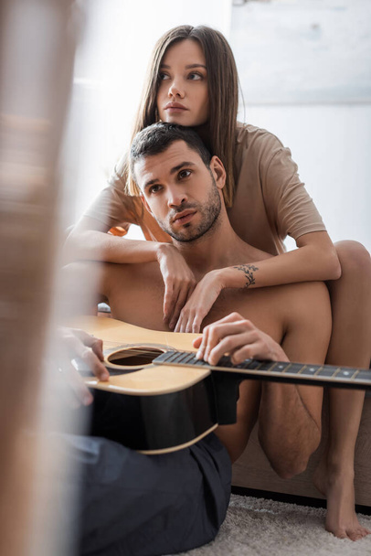 Жінка з Брюнета обіймає сексуального хлопця з акустичною гітарою вдома.  - Фото, зображення