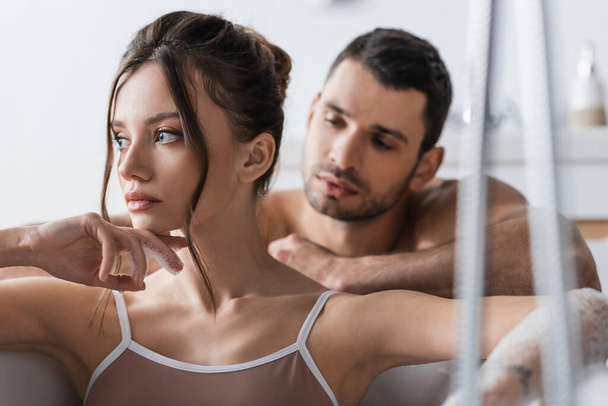 Brunette woman taking bath near blurred shirtless boyfriend at home  - Foto, immagini