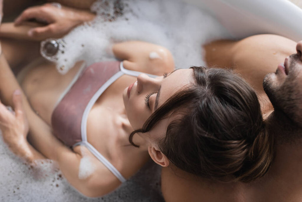 Вид сверху на сексуальную пару, принимающую размытую ванну с пеной дома  - Фото, изображение