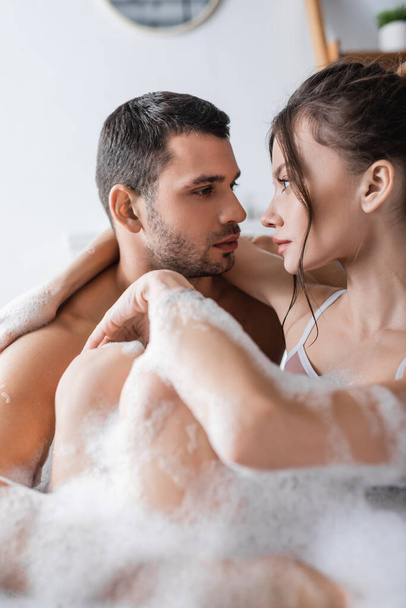 Young couple looking at each other while taking bath with foam at home  - Φωτογραφία, εικόνα