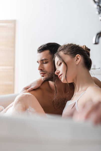 Brunette woman hugging boyfriend in bath with foam at home  - Photo, Image