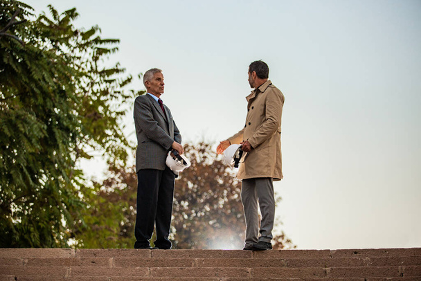 Two senior businessmen are talking while standing on the stairs - 写真・画像